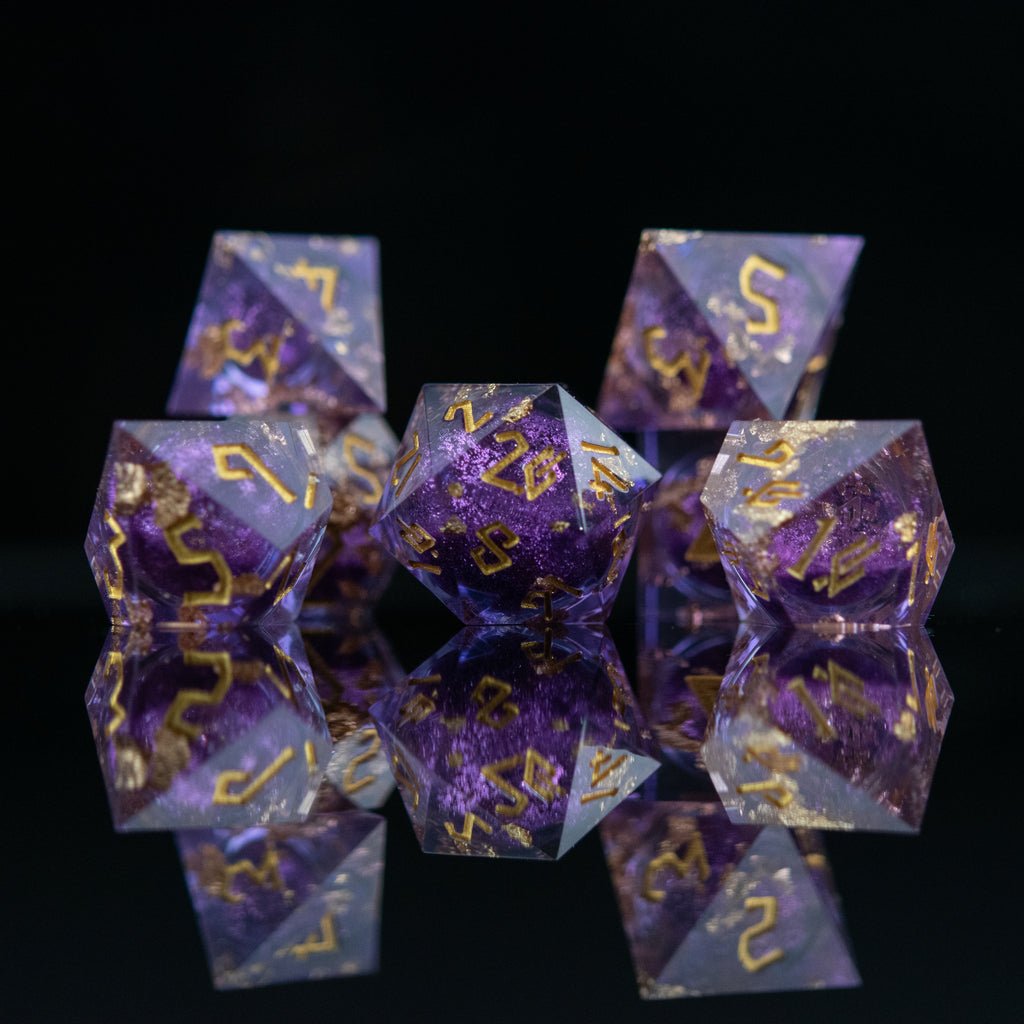 A set of purple resin dice with golden numbers, featuring a liquid core with glitter, arranged on a reflective surface.