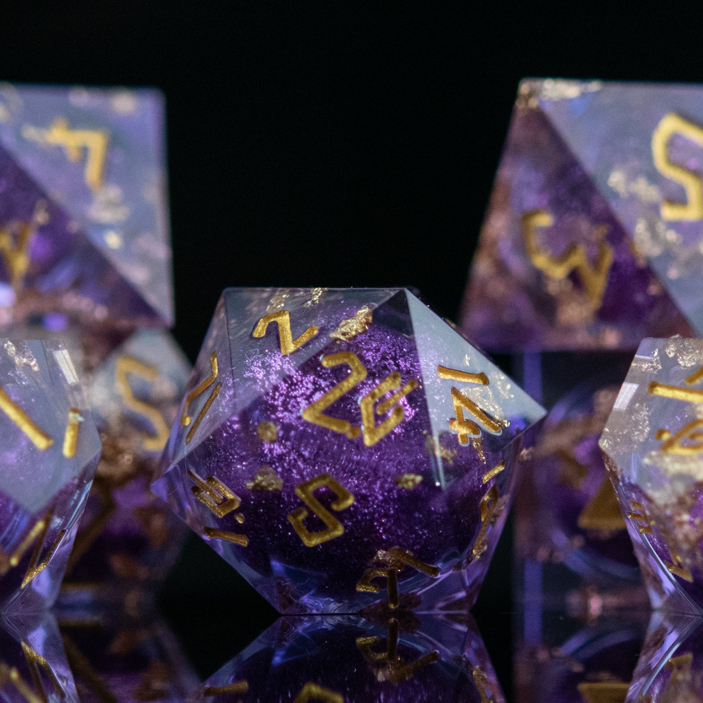 A set of purple resin dice with golden numbers, featuring a liquid core with glitter, arranged on a reflective surface.