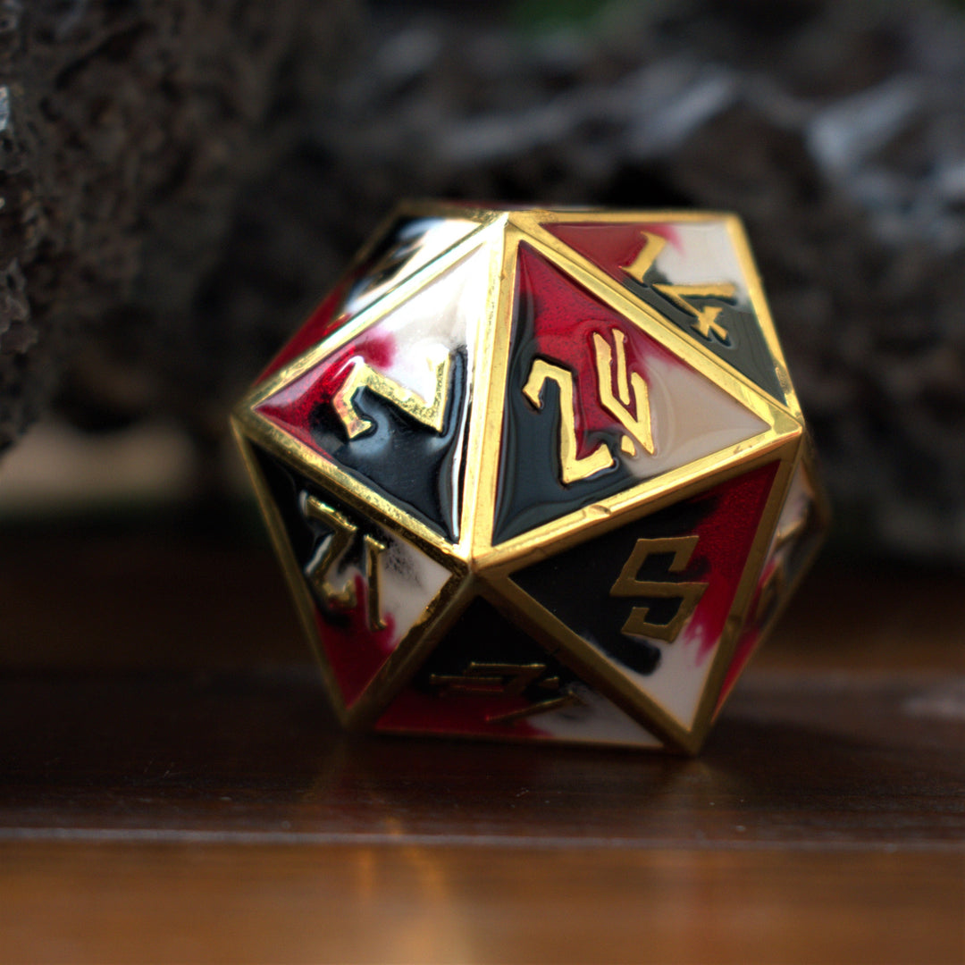 A close-up of a 35mm metal D20 dice with red, black and white colors and gold embossed numbers, placed on a wooden surface.