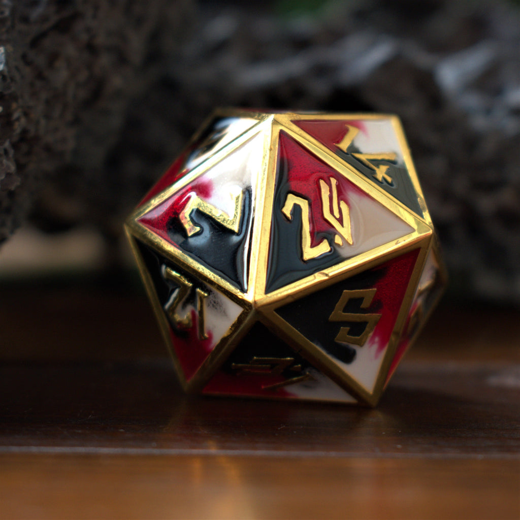 A close-up of a 35mm metal D20 dice with red, black and white colors and gold embossed numbers, placed on a wooden surface.