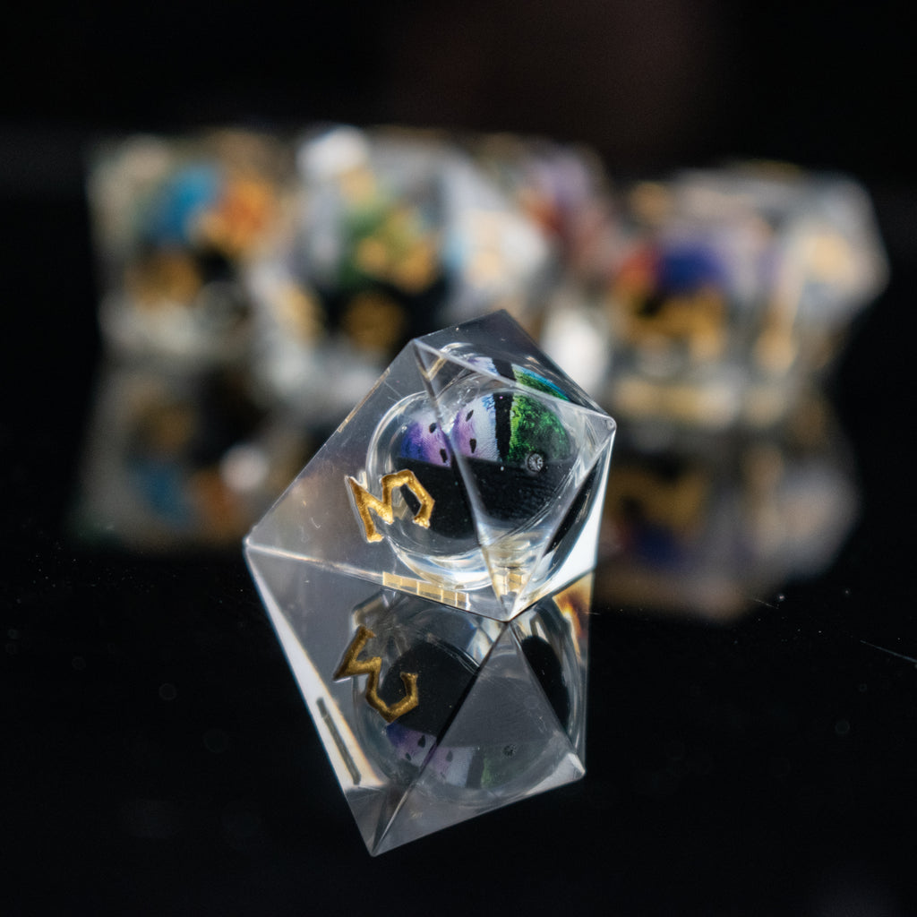 A set of multicolored liquid core resin dice with eye designs inside, displayed on a dark surface.