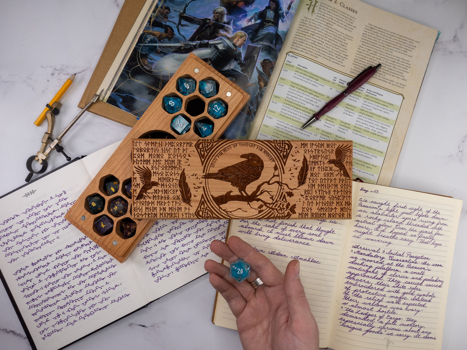 Wooden dice tray with engraved design on top of a notebook with writing and a pen.