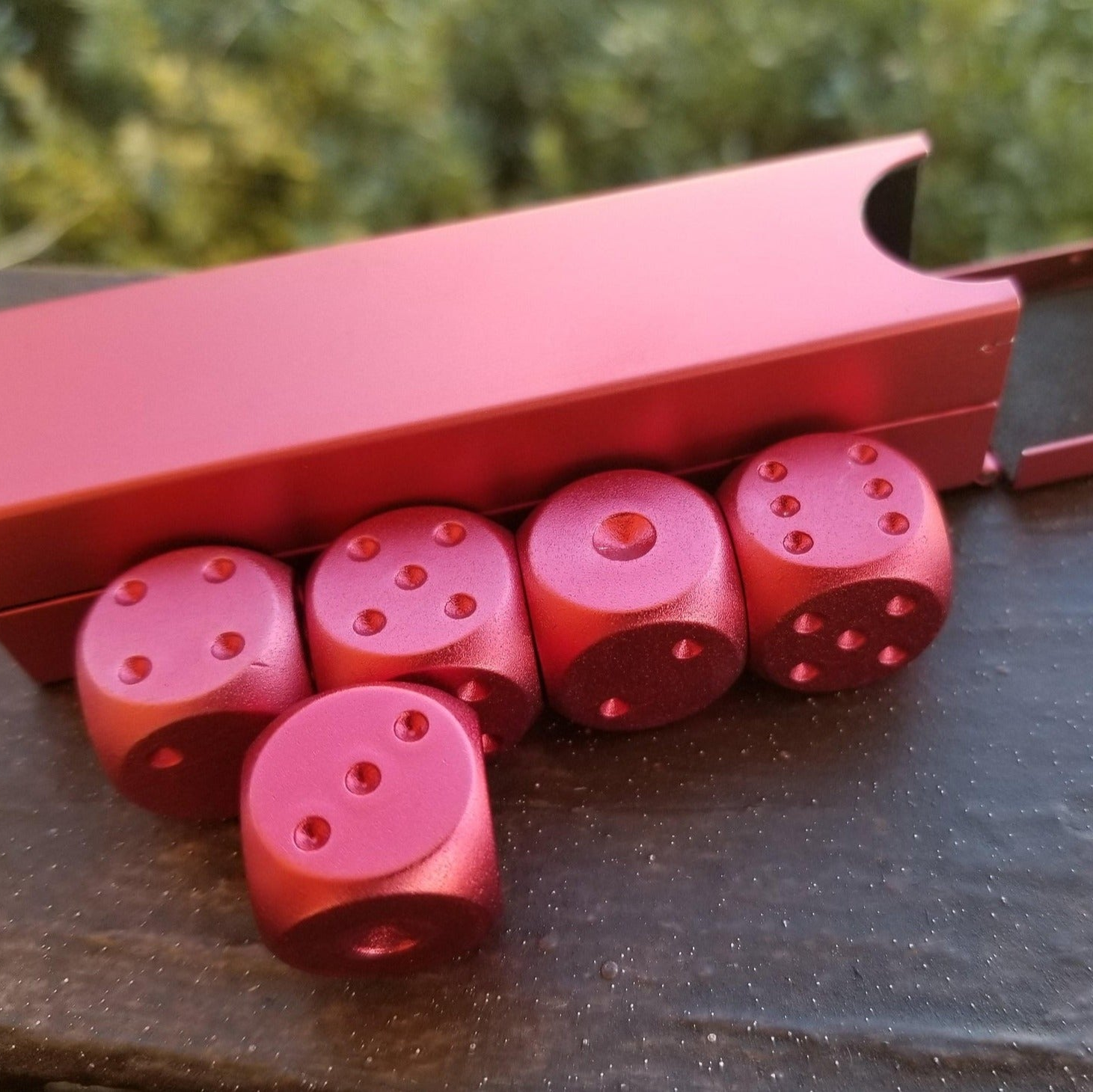 A set of red aluminum D6 dice with engraved numbers, displayed alongside a red foam-lined case.