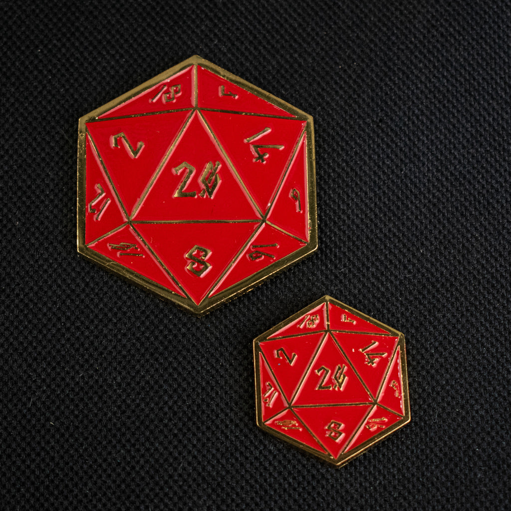 Two enamel pins shaped like D20 dice, with red background and gold numbers, on a black background.