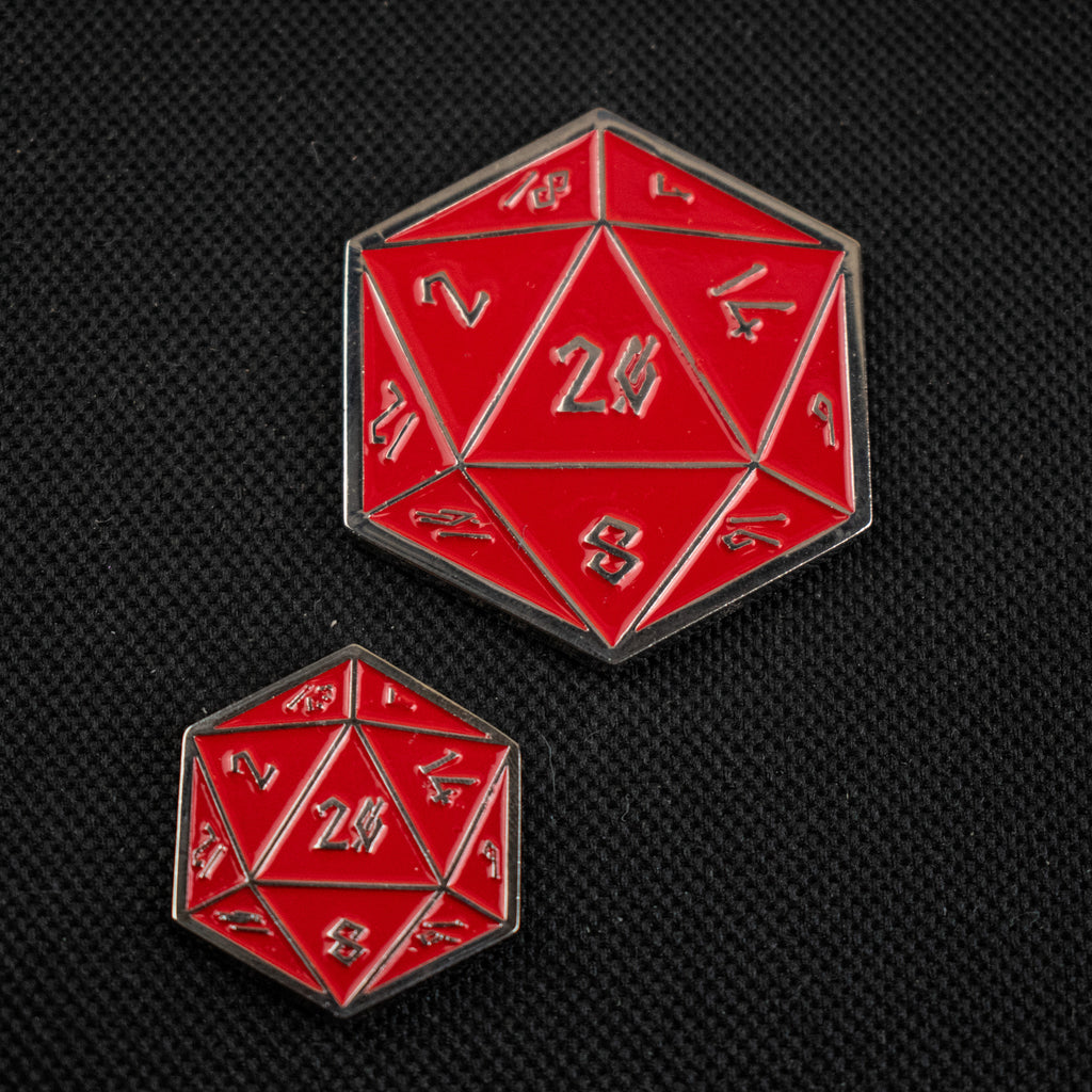Two D20-shaped pins, the larger one in red with silver details and the smaller one in silver with red details, placed on a black background.