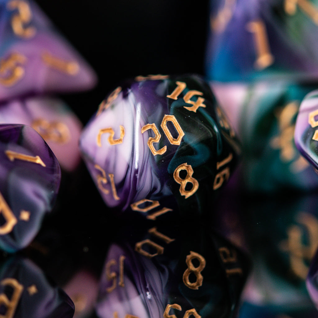 A set of multicolored acrylic dice with engraved gold numbers, displayed on a reflective surface, for tabletop games