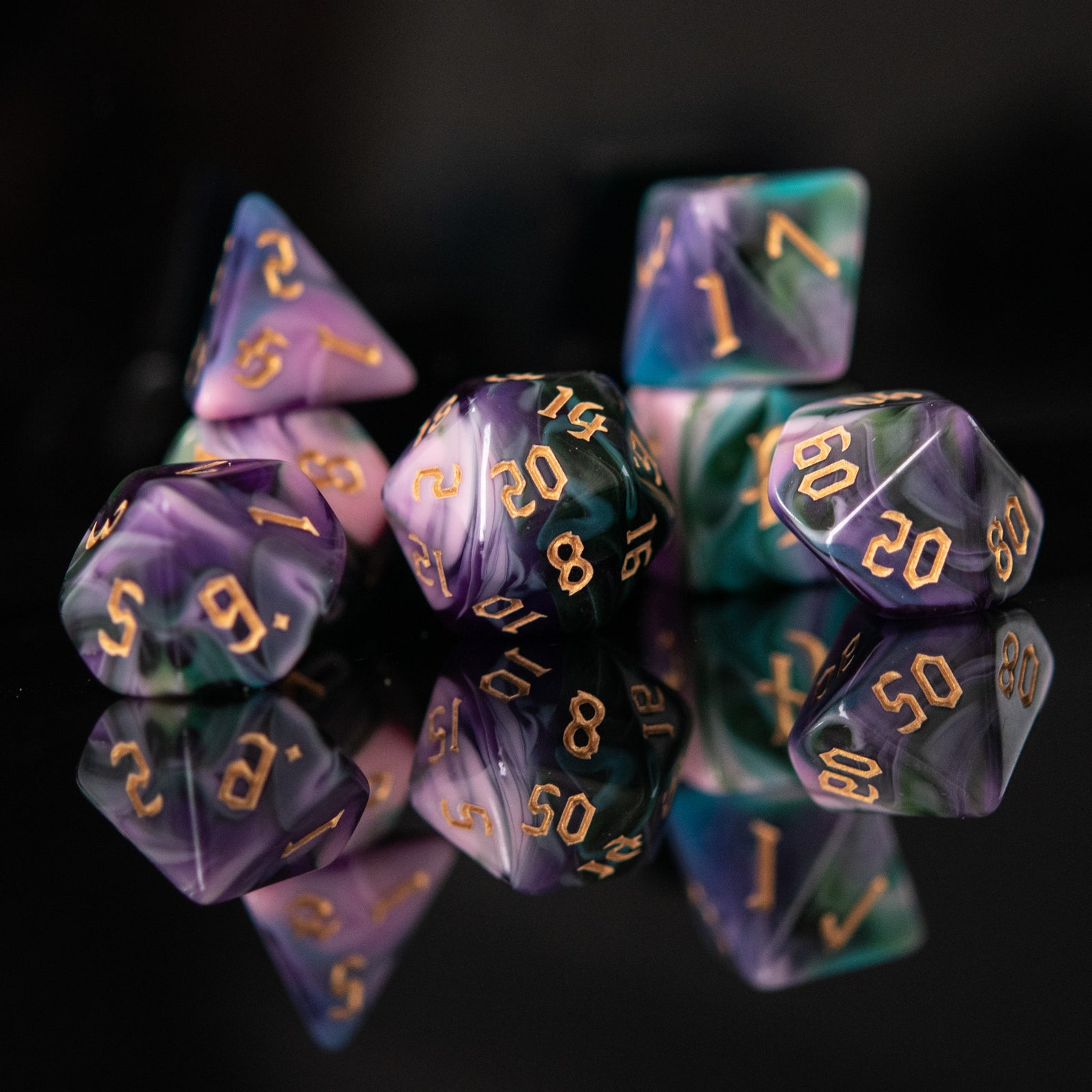A set of multicolored acrylic dice with engraved gold numbers, displayed on a reflective surface, for tabletop games