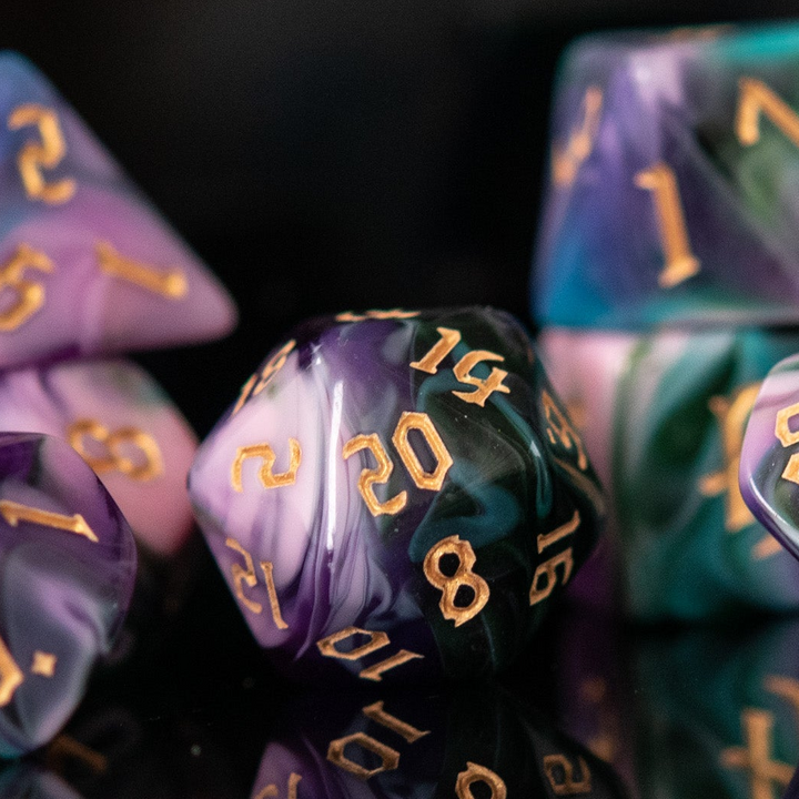 A set of multicolored acrylic dice with engraved gold numbers, displayed on a reflective surface, for tabletop games