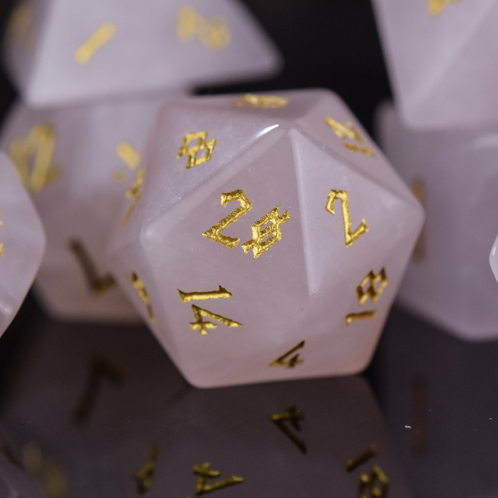A collection of pink rose quartz stone dice with engraved numbers, displayed on a reflective surface.