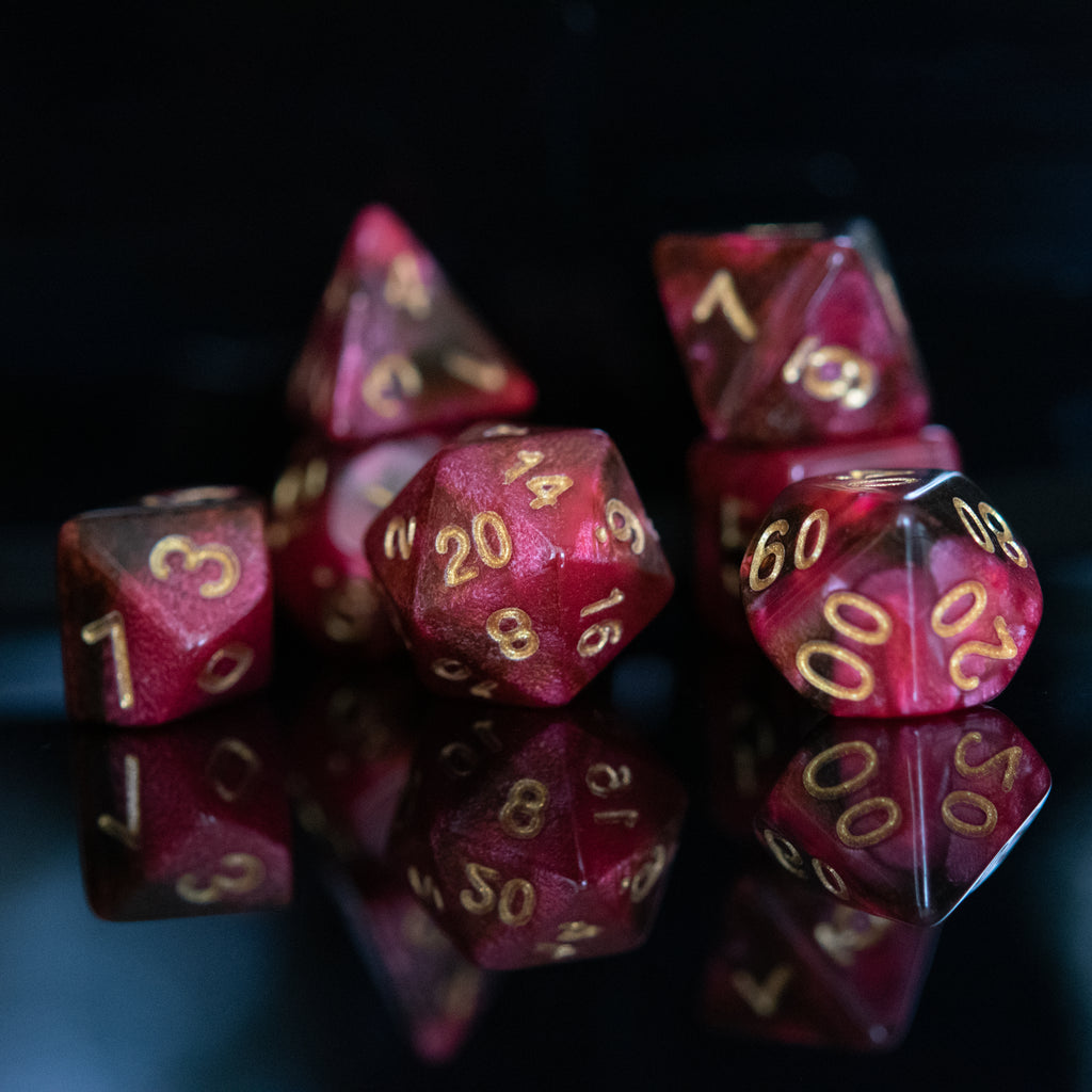 A set of acrylic dice in varying shades of red with engraved numbers in a dark setting, showcasing a variety of dice including a D4, D6, D8, D10, D12, and D20.