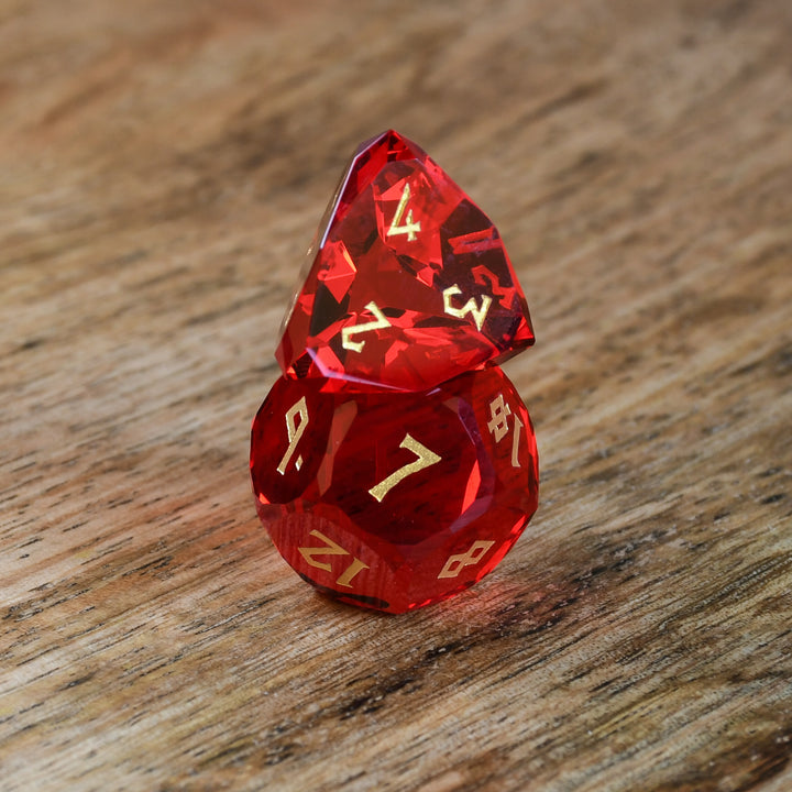 A set of multifaceted red glass dice with engraved numbers, placed on a wooden surface.