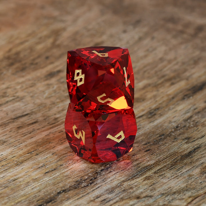 A set of multifaceted red glass dice with engraved numbers, placed on a wooden surface.