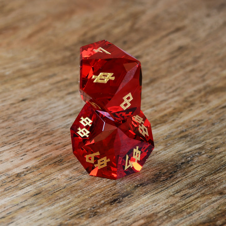 A set of multifaceted red glass dice with engraved numbers, placed on a wooden surface.