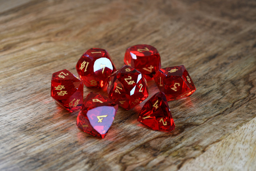 A set of multifaceted red glass dice with engraved numbers, placed on a wooden surface.