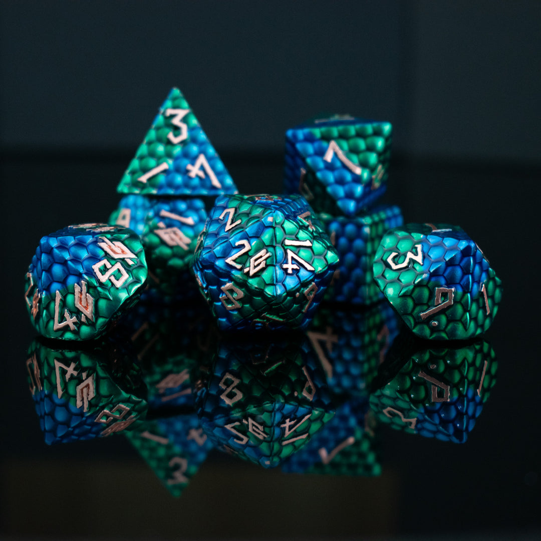 A set of metal dnd dice with blue and green on a dragons egg scale with gold embossed numbers, reflecting on a shiny surface.