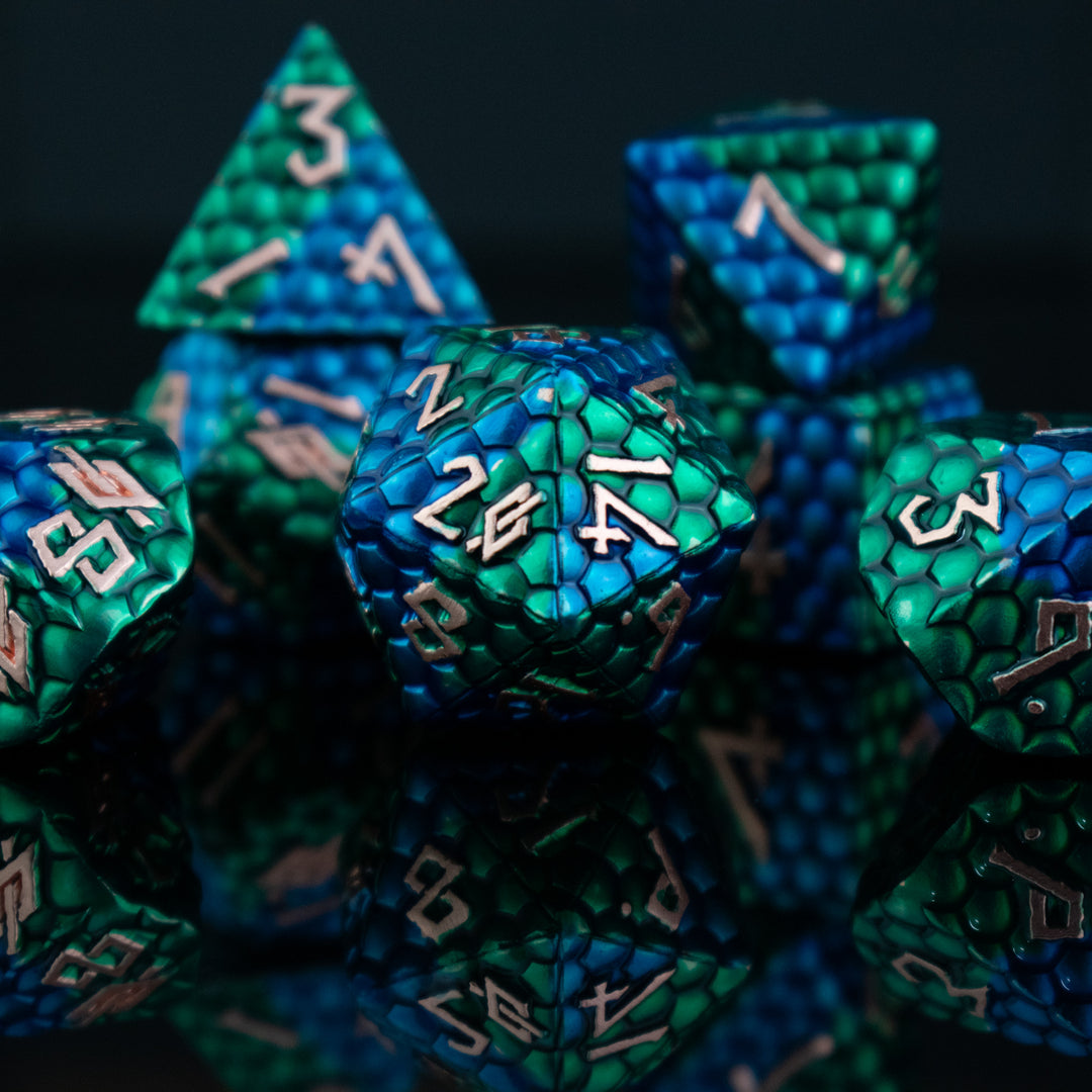 A set of metal dnd dice with blue and green on a dragons egg scale with gold embossed numbers, reflecting on a shiny surface.