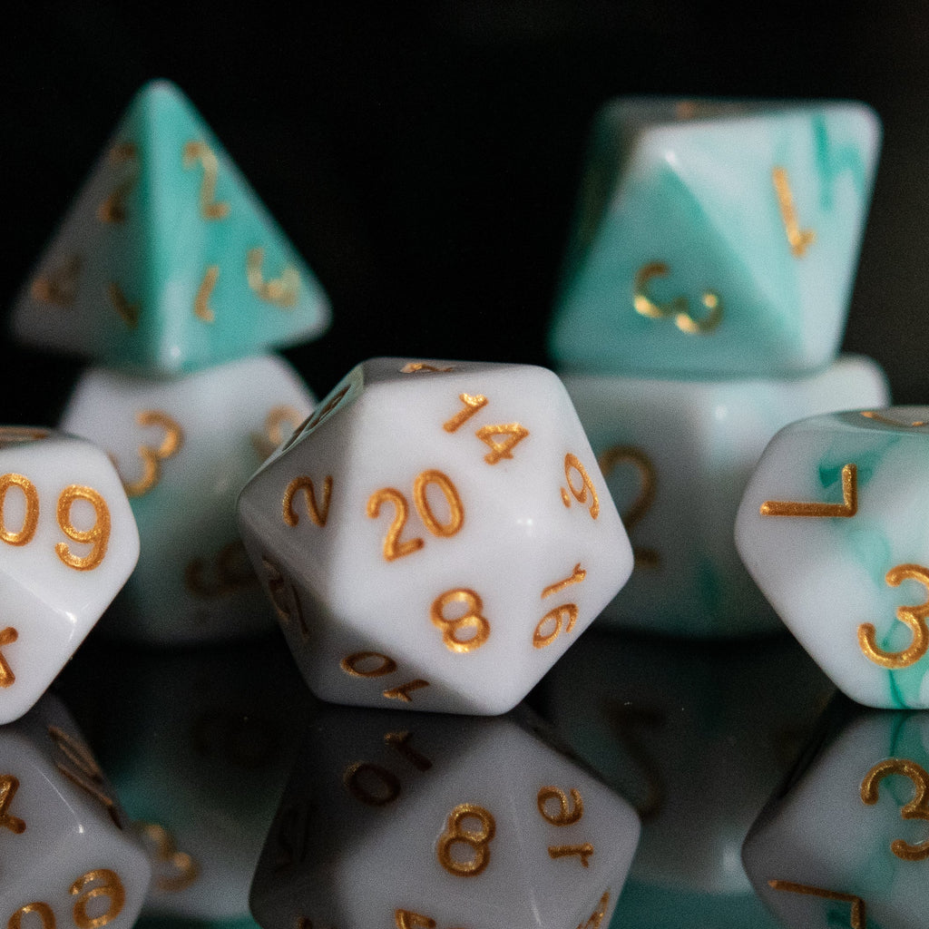 A set of seafoam green and white acrylic dice with engraved numbers, reflecting on a black surface.