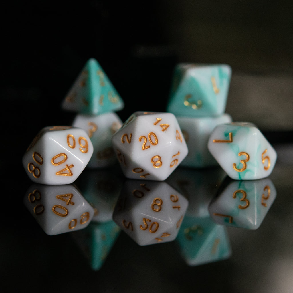A set of seafoam green and white acrylic dice with engraved numbers, reflecting on a black surface.