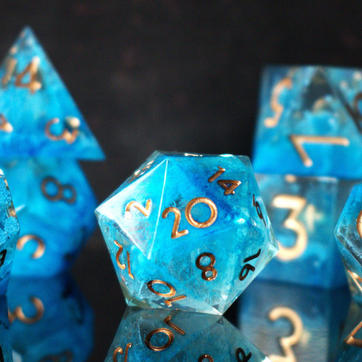 A set of sharp-edged resin dice in blue with gold numbers, including various shapes typical for RPG games.