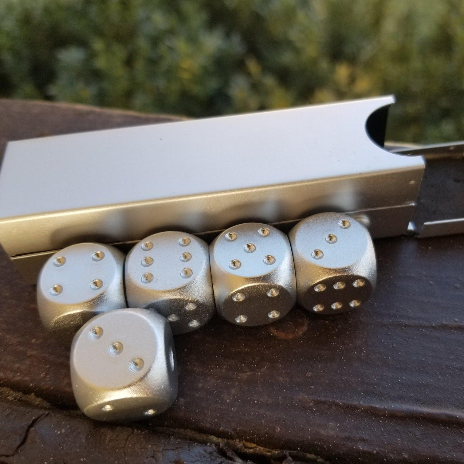 Silver dice with pips and a metal die cutters on a wooden surface