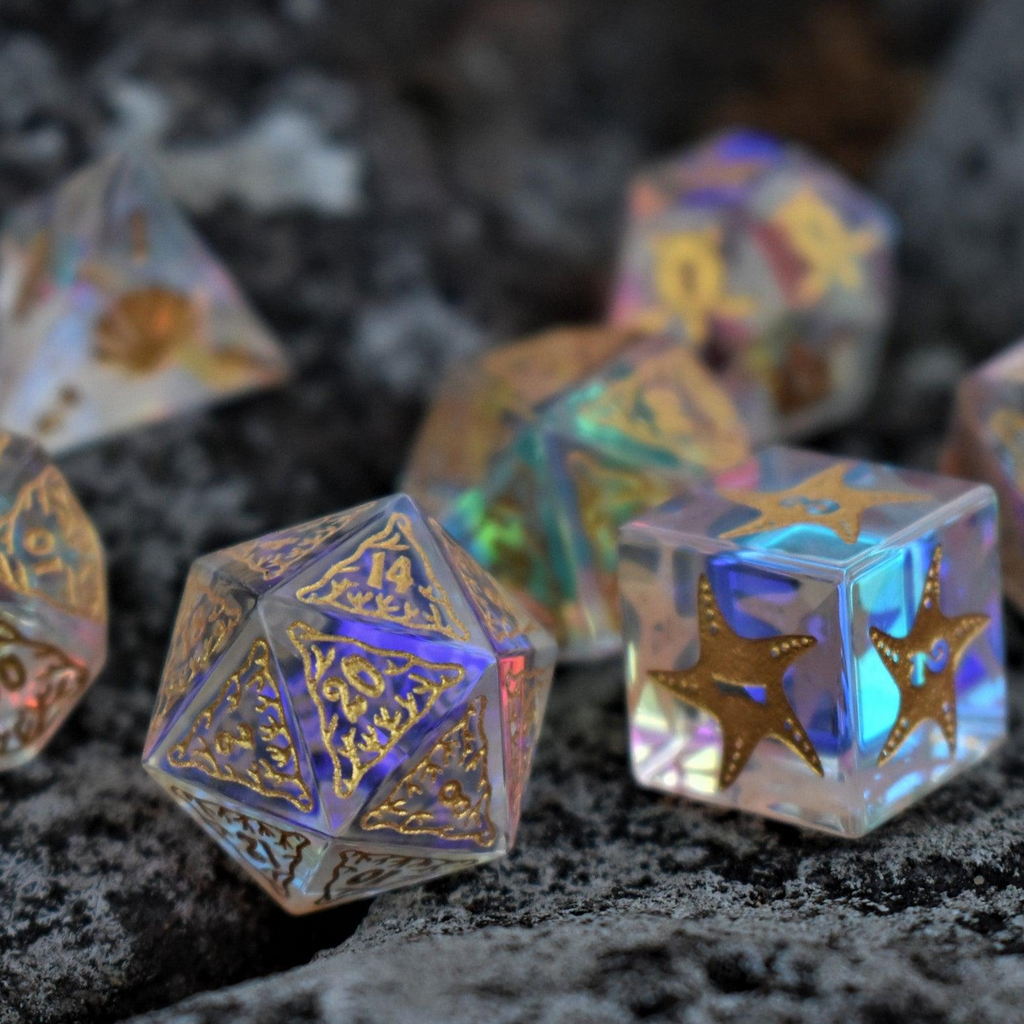 A set of hand-cut, multicolored prismatic glass polyhedral dice with engraved gold numbers and details inspired by the ocean on each face.