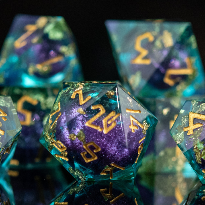 A set of resin core dice with purple and green colors, featuring engraved numbers and floating glitter, displayed on a reflective surface.