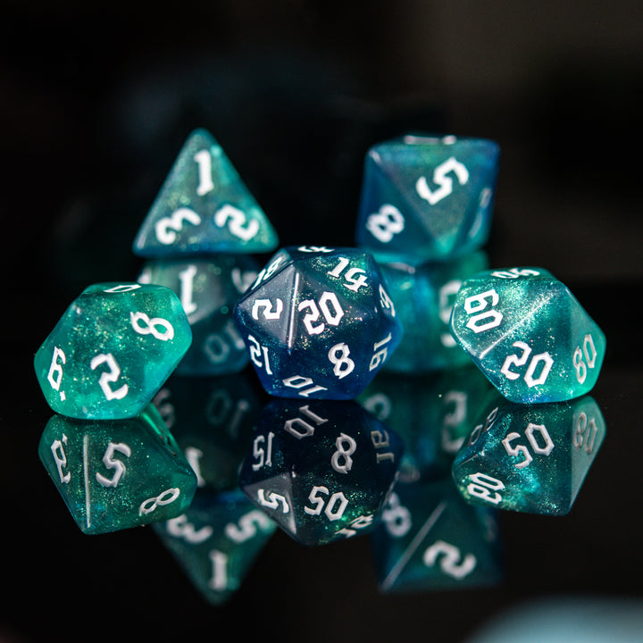 A set of acrylic dice in varying shades of blue and green with white numbers, displaying a variety of numbers from D4 to D20.