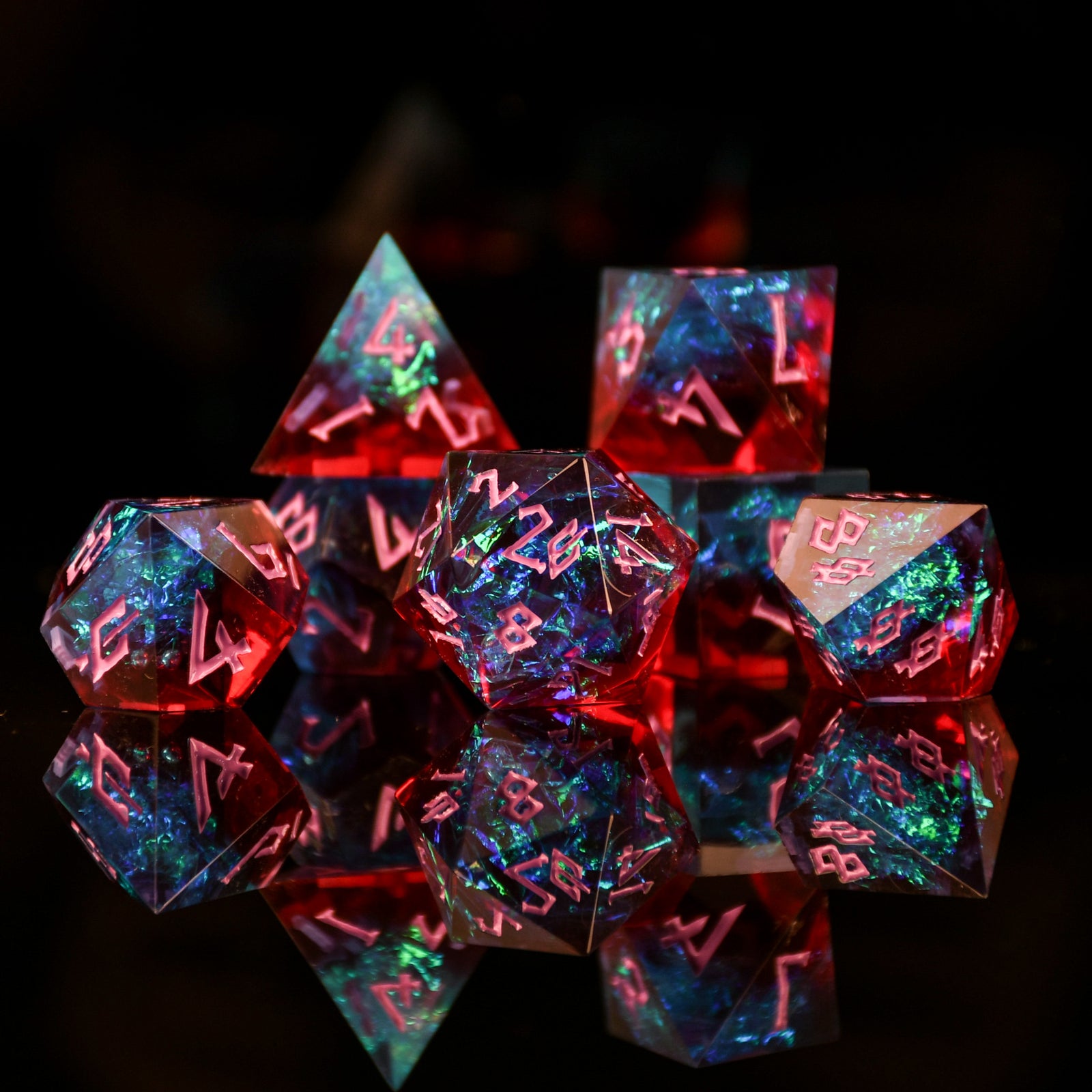 A set of sharp-edged resin dnd dice in red and blue colors with hand-painted pink numbers and irridescent foil inside, reflecting on a surface.