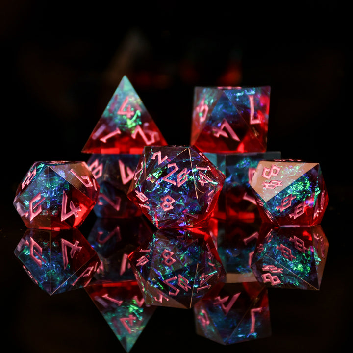 A set of sharp-edged resin dnd dice in red and blue colors with hand-painted pink numbers and irridescent foil inside, reflecting on a surface.