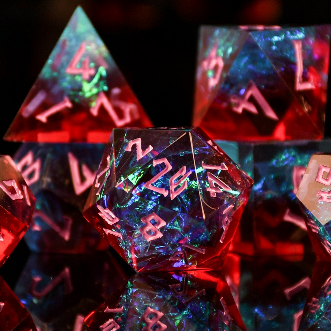 A set of sharp-edged resin dnd dice in red and blue colors with hand-painted pink numbers and irridescent foil inside, reflecting on a surface.