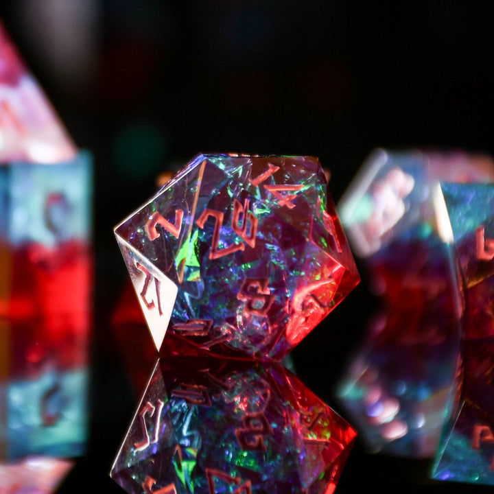 A set of sharp-edged resin dnd dice in red and blue colors with hand-painted pink numbers and irridescent foil inside, reflecting on a surface.