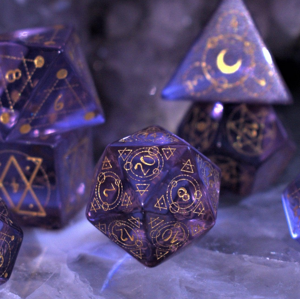 A set of purple glass dice with engraved golden numbering and details for tabletop gaming and collectors