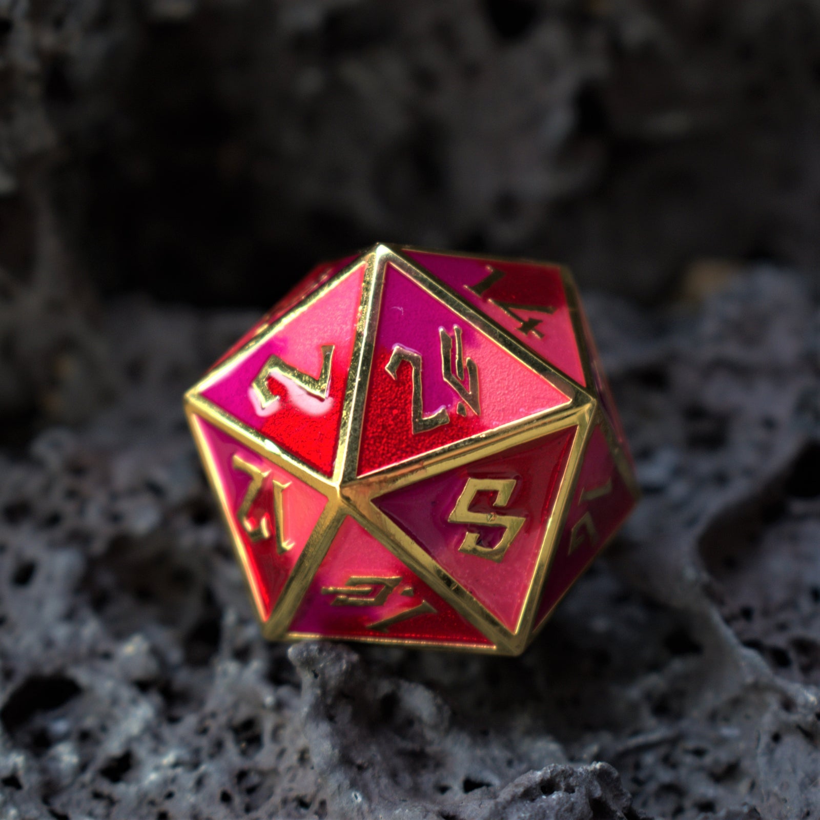 A close-up of a pink and gold metal D20 gaming die with embossed numbers, placed on a textured dark background.