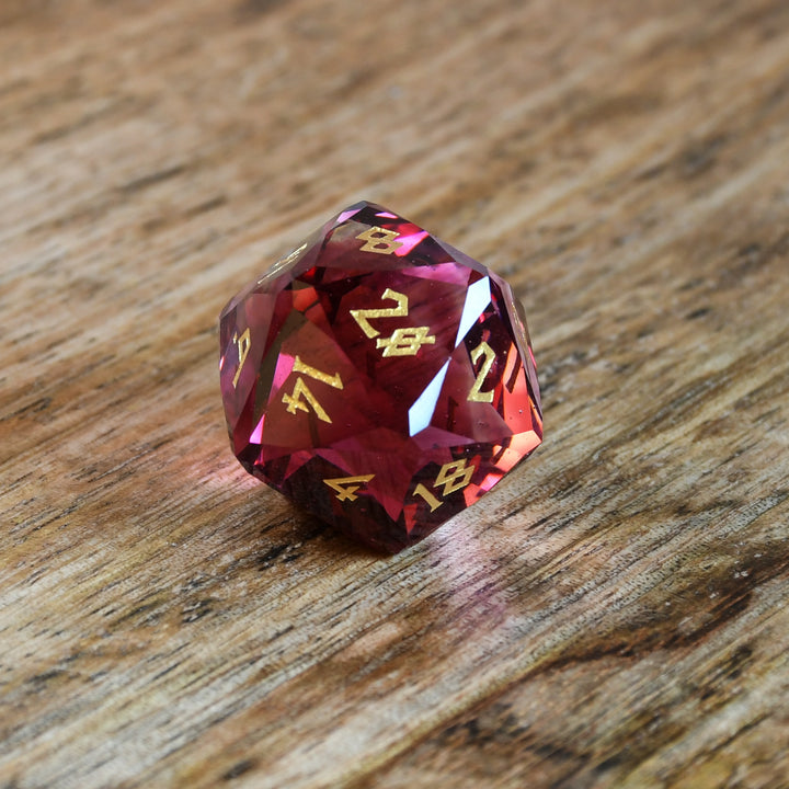 A set of multifaceted cut glass dnd dice with engraved numbers, displayed on a wooden surface. The dice are primarily red with gold text