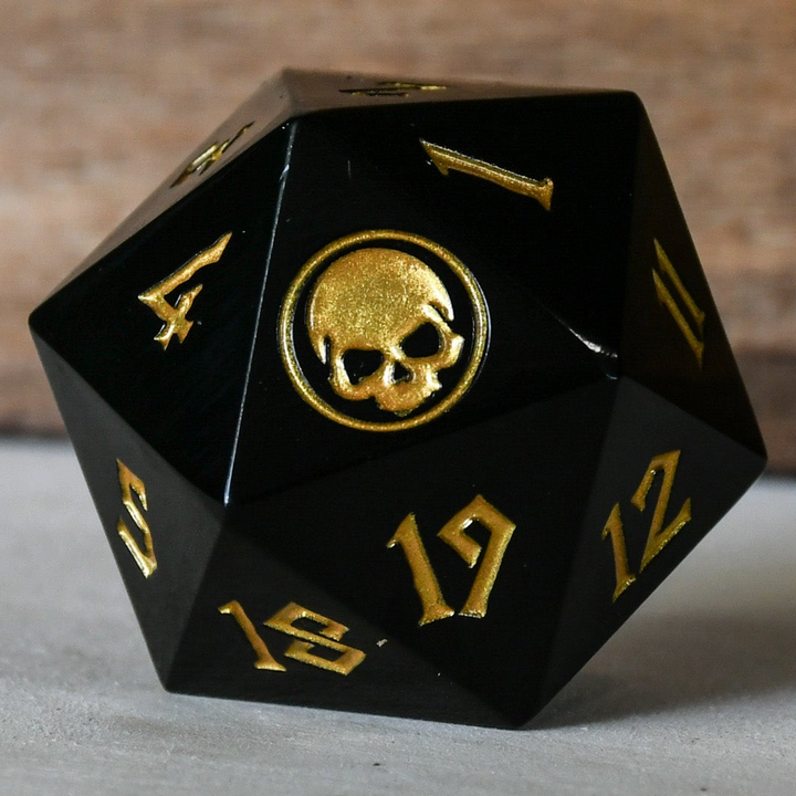 An oversized solid-metal black d20 spindown life counter die with gold numbers and an iconography designed for TCG gameplay.