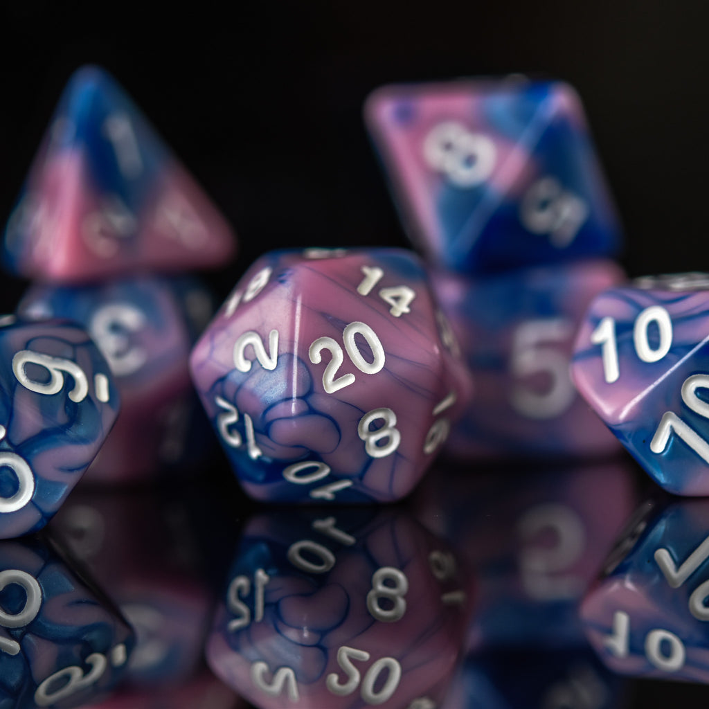A set of hand-carved blue and pink acrylic dice with engraved numbers, displayed on a reflective surface.