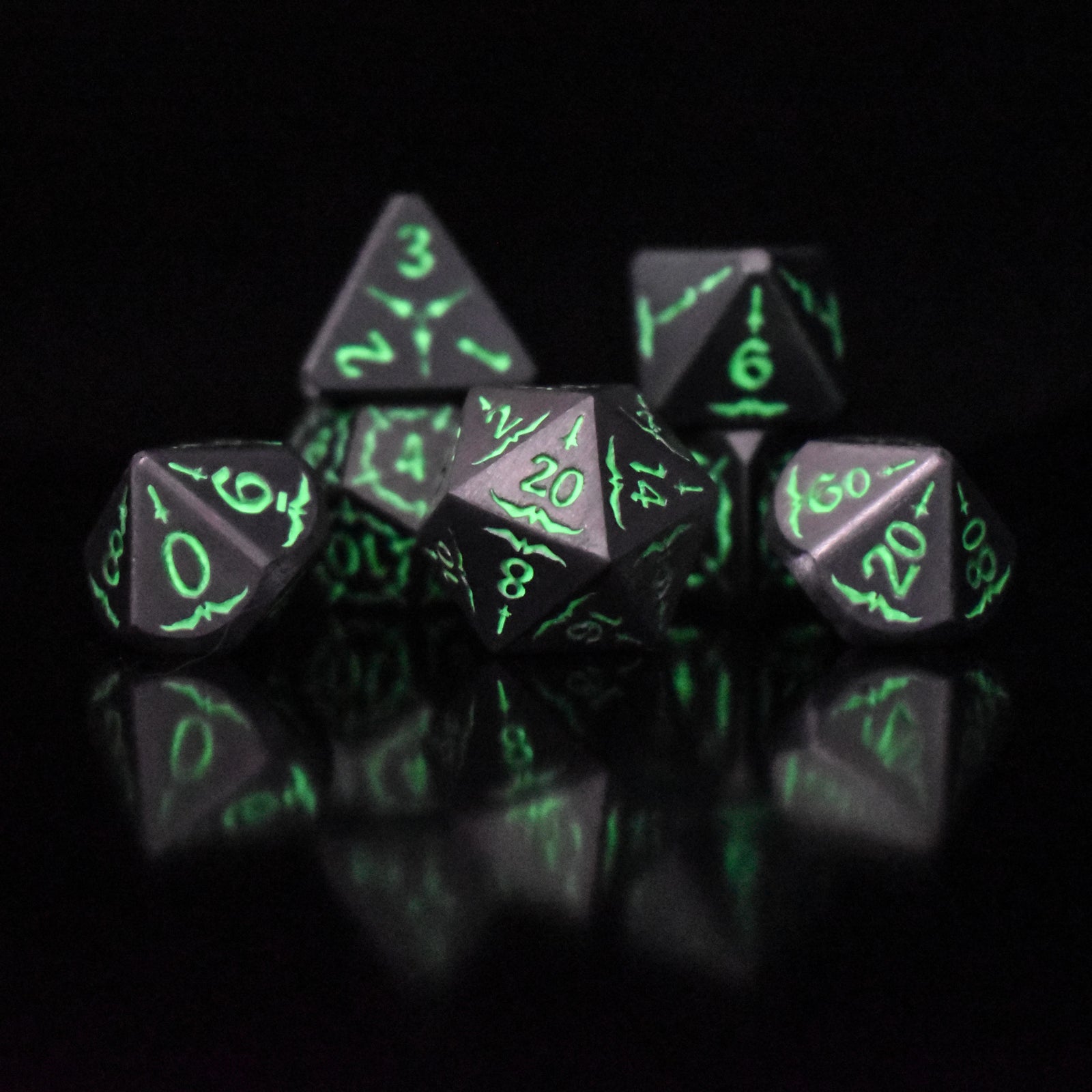 A set of glow-in-the-dark metal dnd dice with engraved numbers and swords, including various shapes such as a d4, d6, d8, d10, d12, and d20, displayed on a black background.