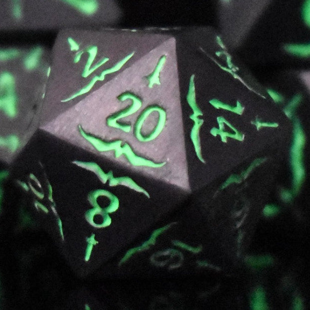 A set of glow-in-the-dark metal dice with engraved numbers, including various shapes such as a d4, d6, d8, d10, d12, and d20, displayed on a black background.