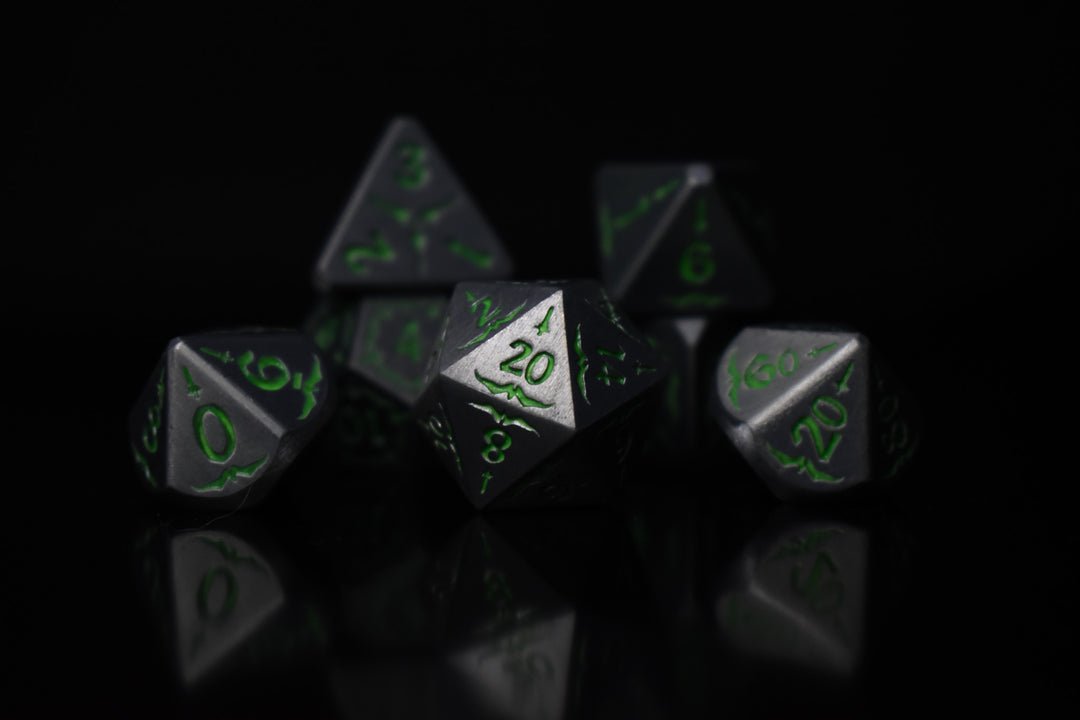 A set of glow-in-the-dark metal dnd dice with engraved numbers and swords, including various shapes such as a d4, d6, d8, d10, d12, and d20, displayed on a black background.
