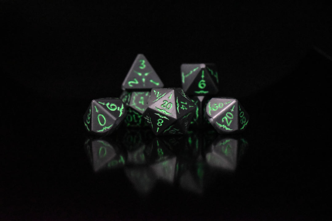 A set of glow-in-the-dark metal dnd dice with engraved numbers and swords, including various shapes such as a d4, d6, d8, d10, d12, and d20, displayed on a black background.
