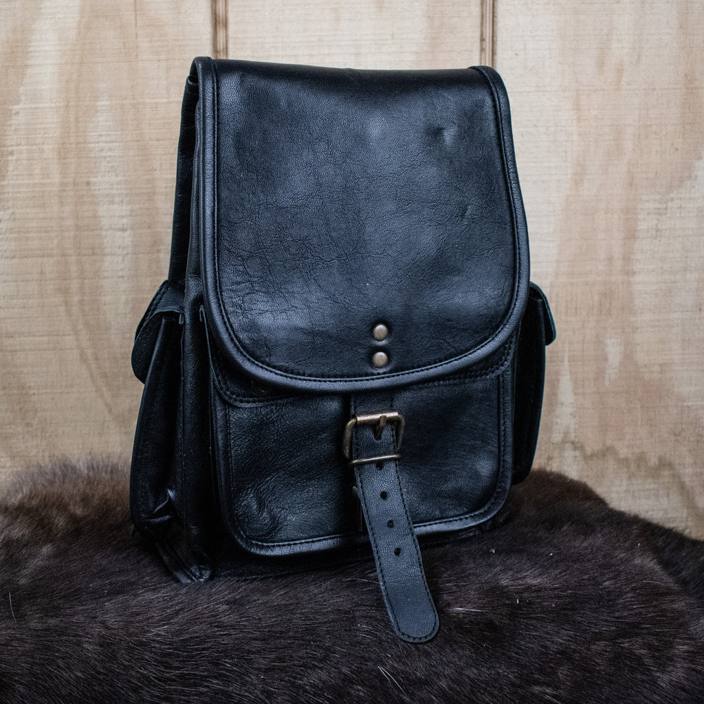 A black leather mini backpack with brass hardware, displayed against a wooden background.