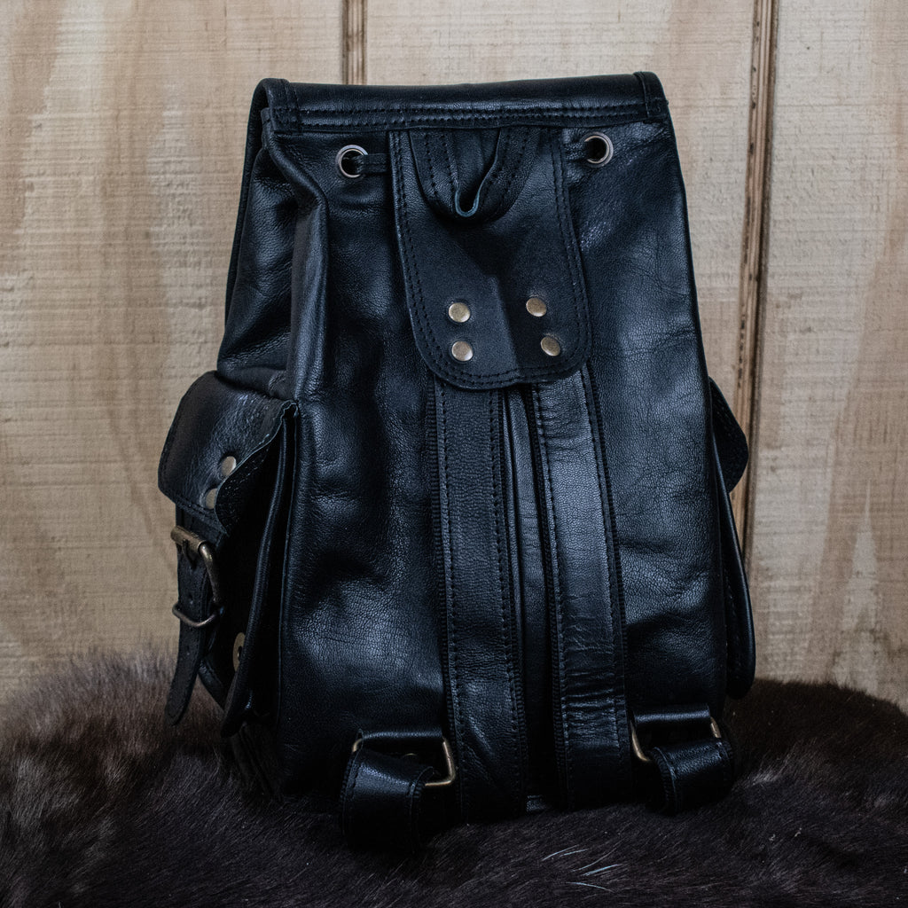 A black leather mini backpack with brass hardware, displayed against a wooden background.