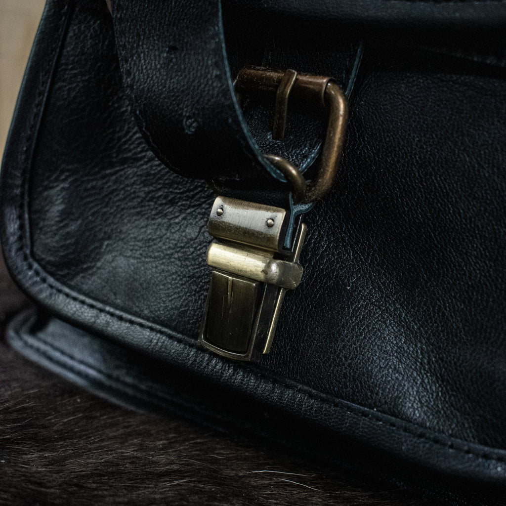 A black leather mini backpack with brass hardware, displayed against a wooden background.