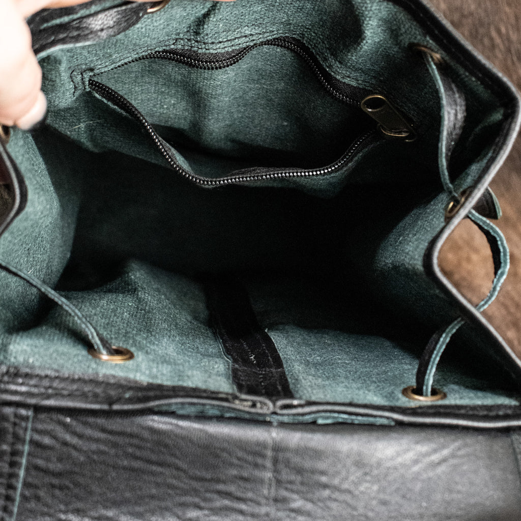A black leather mini backpack with brass hardware, displayed against a wooden background.