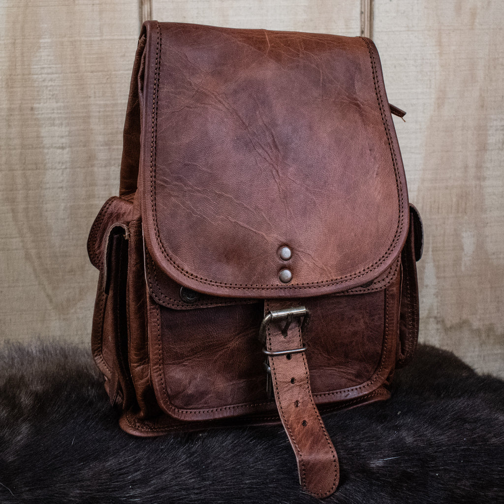 A brown leather mini backpack with brass zippers and a canvas lining, displayed against a textured background.