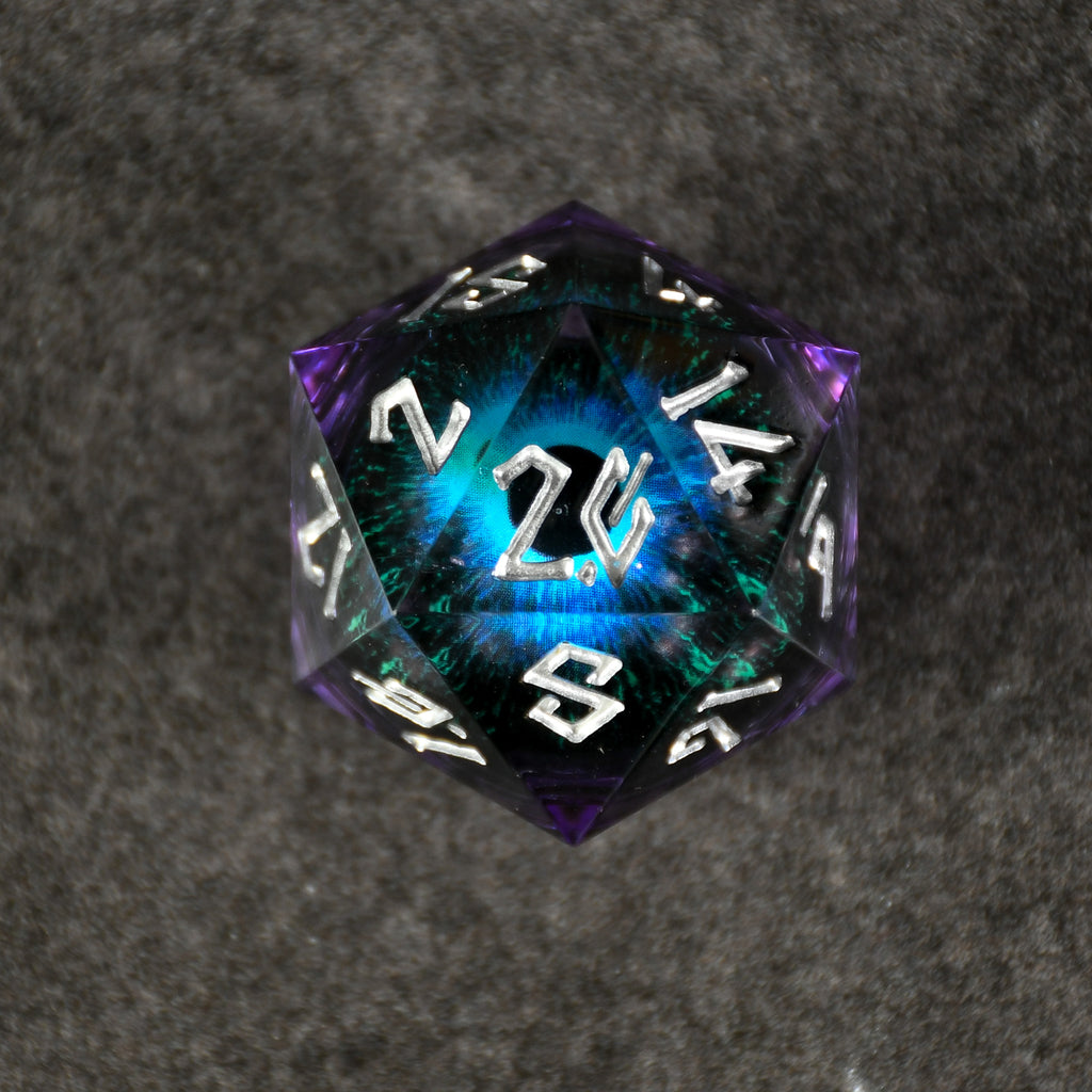 A large, multicolored resin dice with engraved numbers and a floating eye illustration inside, set against a textured grey background.