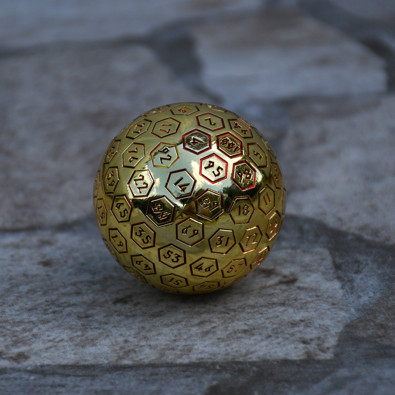 A red and gold oversized metal D100 dice with engraved numbers on a textured background.