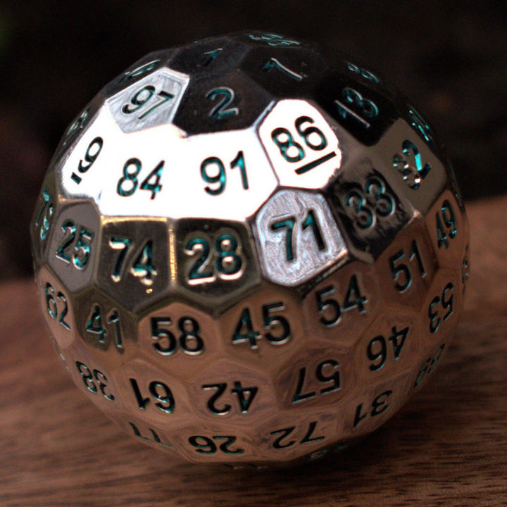 A large silver metal d100 dice with engraved aqua numbers, resting on a wooden surface.