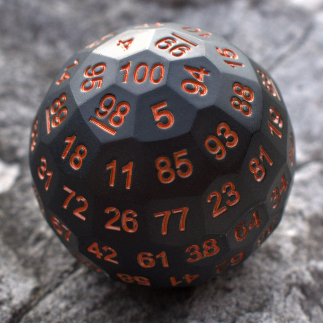 A large black metal dice, a D100, with engraved orange numbers, resting on a rocky surface.
