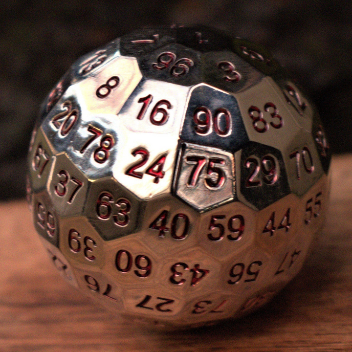 A large silver metal d100 dice with red engraved numbers, resting on a wooden surface for wargaming tabletop gaming board games